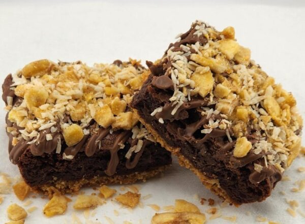Two chocolate brownies topped with nuts and drizzled with caramel on a white background.