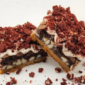 Two pieces of layered dessert bars with cookie crumble topping on a white surface.