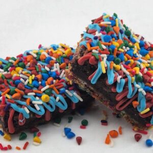 Two sprinkle-covered brownies on a white surface.