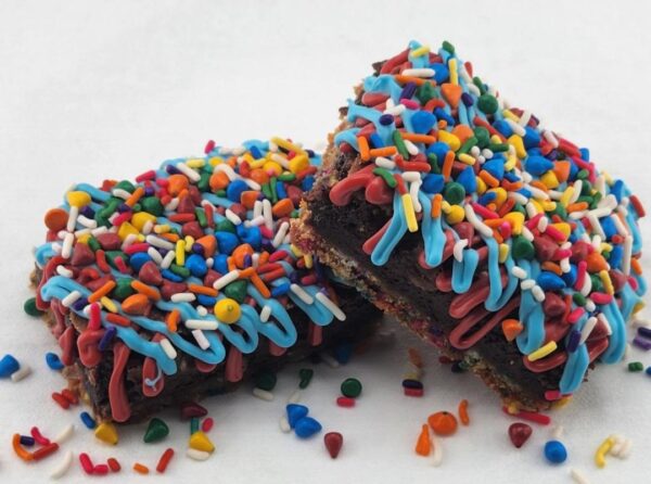 Two sprinkle-covered brownies on a white surface.