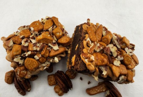 Chocolate brownies covered with nuts and pretzels, sliced in half, on a white surface.