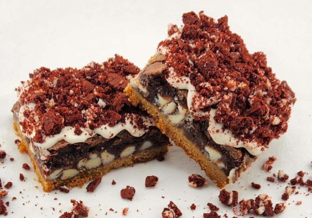 Two pieces of layered dessert bars with cookie crumble topping on a white surface.